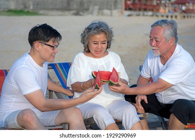 Concept Of Relaxation On Vacation. Asian Family Picnic On The Beach With Delicious Watermelon On Chairs. They Are Happy And Rested In The Summer During The Holidays.