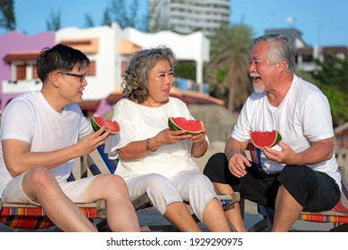 Concept Of Relaxation On Vacation. Asian Family Picnic On The Beach With Delicious Watermelon On Chairs. They Are Happy And Rested In The Summer During The Holidays.