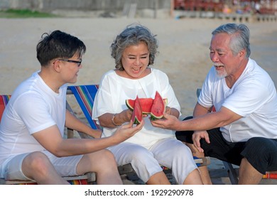 Concept Of Relaxation On Vacation. Asian Family Picnic On The Beach With Delicious Watermelon On Chairs. They Are Happy And Rested In The Summer During The Holidays.