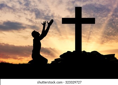 concept of religion. Silhouette of a man praying before a cross at sunset