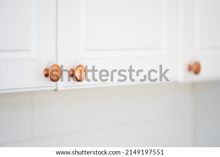 Concept of renovation, replacement detail. Selective focus at round copper door handles on white cabinet in classic style. Close up of new knob on kitchen furniture, blurred copy space background