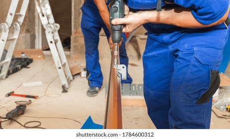 Concept Of Replacement Details. Panoramic And Cropped View Of Two Professional Workers Install Metal Rail On Garage Door System In New House Under Construction, Using Electric Screwdriver