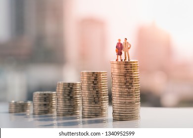Concept of retirement planning. Miniature people: Old couple figure standing on top of coin stack.