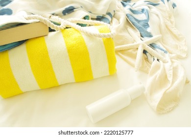 Concept of retreat, travel, vacation, summer, beach, good day, sun bathing, hotel, spa. On white bed lies striped yellow towel, bag with book, silk sundress, sunscreen and starfish. Nobody. Copy space - Shutterstock ID 2220125777