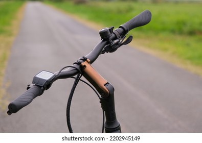 Concept riding a bike alone in nature: close-up of a bicycle handlebar of an e-bike in the foreground, bike path and green nature in the blurred background