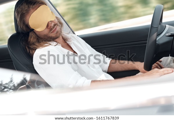 Concept of safety travel on\
automobile. Side view of young adult man wearing in sleeping mask,\
taking nap in comfort and new modern car, making pause after long\
ride