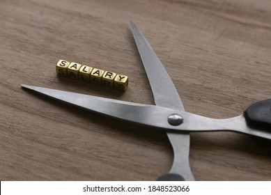 Concept Of Salary Cut. Selective Focus Of Scissors And Gold Alphabet Beads Of Word Salary On Wooden Background.