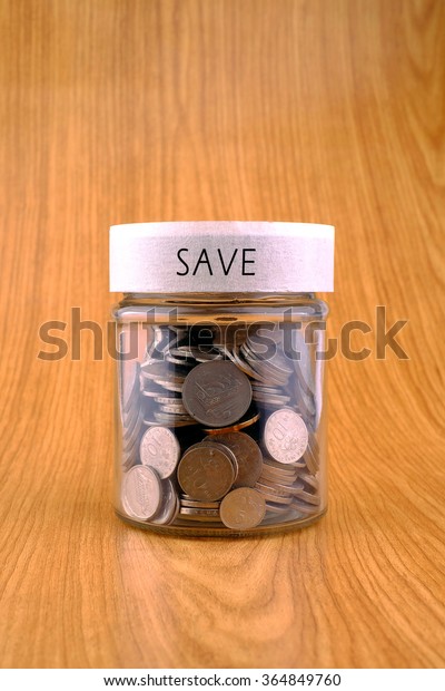 concept of saving, coins in jar with save\
label on wooden\
background.