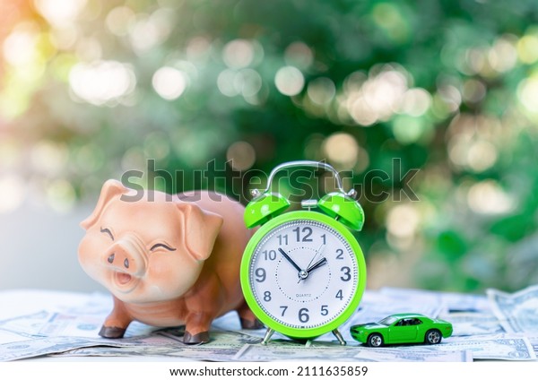 Concept of\
saving, finance and investment with piggy bank, alarm clock and car\
model on blur green plant\
background.