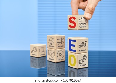 The concept of search engine optimization. A man's hand sets a wooden cube on top, on the cubes the SEO inscription and icons with the image and inscription of various actions and events. - Shutterstock ID 1707918067