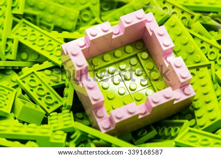 Concept of selective focus on secured and protected green area within wall constructed using building blocks, against heaps of green bricks