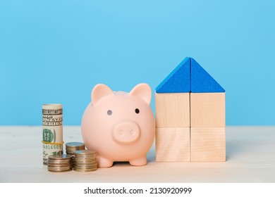 The concept of selling a house and real estate. Toy house made of wooden cubes , piggy bank and dollar bills on a blue background