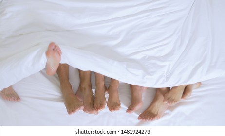 Concept Sex clubs, swing clubs, lifestyle clubs, formal, informal groups. feet of a group of people under a white blanket on a white sheet on a king size bed