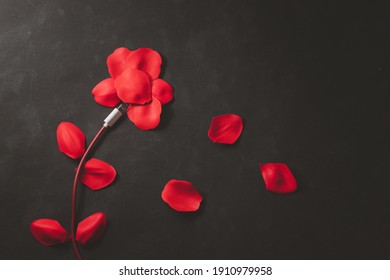 Concept shape, love, technology Red smartphone charging cable and rose petals on black background - Powered by Shutterstock