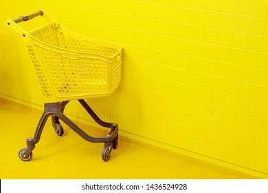 The concept of shopping. An empty yellow grocery cart stands on a yellow floor against the background of a yellow wall.