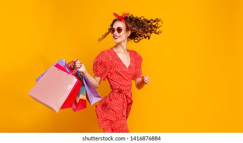 concept of shopping purchases and sales of happy young girl with packages in red dress on yellow background