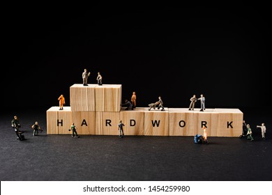 Concept Shot For Hardwork. Miniature Builder Figures Around Wooden Blocks With “HARDWORK” Wordings