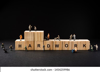 Concept Shot For Hardwork. Miniature Builder Figures Around Wooden Blocks With “HARDWORK” Wordings