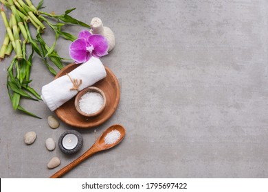 Concept for spa setting with rolled towel and branch orchid.salt on wooden bowl ,with,green bamboo leaf stone,candle, stone on gray background, Copy space - Powered by Shutterstock