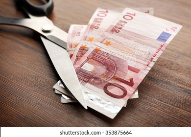 Concept Of Spending Money - Scissors Cut Money On Wooden Background