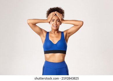 Concept Of Sport And Workout. Distressed And Anxious African-american Female Athlete, Wearing Blue Sportswear, Holding Hands On Head And Panicking, Standing Sad Against White Background