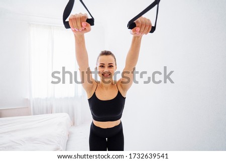 Concept of sports without a gym and sports simulators. Muscular girl fitness trainer showing how exercise at home with a tubular red expander. She ties it to the door and holding it by feets