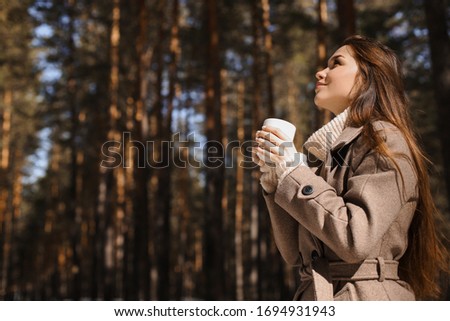 The concept of spring warmth, atmosphere and comfort. With a place for inscription. A beautiful girl drinks hot tea, hot chocolate, coffee in a warm spring forest.