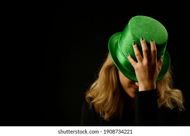 Concept Of St. Patrick. Close Up Of A Woman With Face Covered By A Green Hat, Hand Holding Hat, In A Black Background, Place For Text.