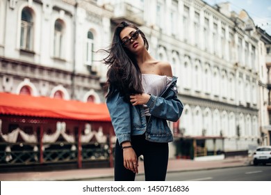 The concept of street fashion. Young beautiful model in the city. Dynamically young girl walks down the street.Hair fluttering in the wind