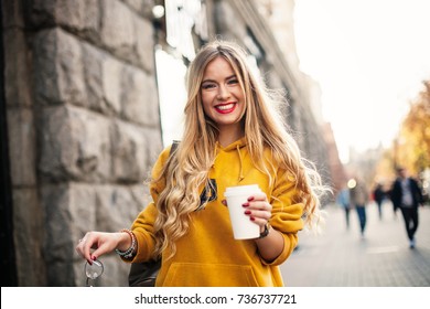 O conceito de moda de rua. jovem estudante menina elegante vestindo jeans namorado, tênis branco moletom amarelo brilhante.Ela segura café para ir. retrato de menina sorridente em óculos de sol e com saco