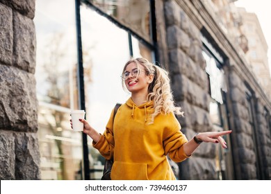 The concept of street fashion. young stylish girl student wearing boyfriend jeans, white sneakers bright yellow sweatshirt.She holds coffee to go and dance .