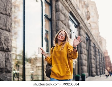 The concept of street fashion. young stylish girl student wearing boyfrend jeans, white sneakers bright yellow sweetshot.She holds coffee to go and dance .