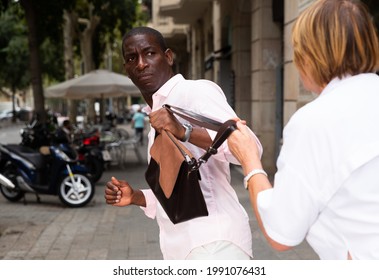 Concept of street theft. Man snatching bag of frightened elderly woman on city street