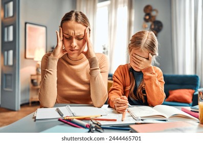 Concept of stressful parenthood. Frustrated mum keeping hands on temples with closed eyes next to daughter hiding face behind arm. Woman becoming hopeless while girl having difficulties with homework. - Powered by Shutterstock