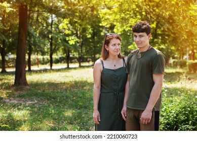 Concept Of Strong Family Relationship Between Mother And Son. A Woman And Her Adult Teenage Son Are Walking In The Park And Talking