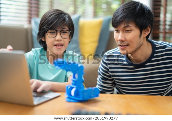 Concept of study at home,coding control\
robotics and home school.asian boy child with father successful\
control robot arm on laptop.happy family getting a lesson of coding\
control robotics\
technology