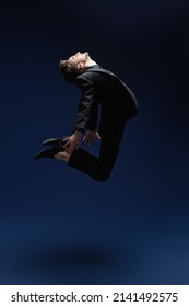The concept of success and aspirations, dreams. A man in a black classic suit jumps, striving for the heights. Studio full-length portrait on a dark blue background. Success in business.