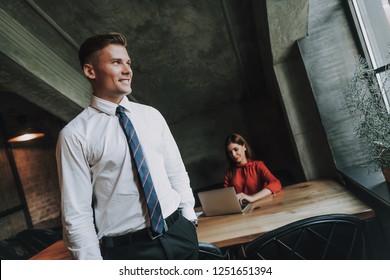 Concept Of Successful Team Work. Waist Up Portrait Of Smiling Confident Business Man Looking At Window While His Female Partner Sitting On Working Table