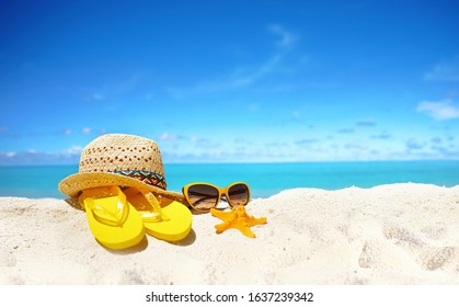 Concept summer beach holiday. Beach accessories - straw hat, glasses, starfish, yellow flip-flops on sandy tropical beach against blue sky with clouds on bright sunny day. Beautiful colorful image. - Powered by Shutterstock