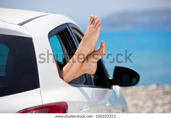 Concept of summer car trip vacation . Woman legs\
out the window in car at background of sea water. Conceptual travel\
,freedom and holidays\
image.