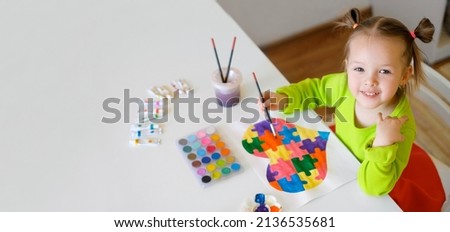 Concept of support for children with autism syndrome. Little girl draws a drawing with a picture of a heart from a puzzle with watercolor paints. Painting lessons. Baby at the table holds a paintbrush