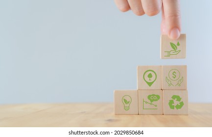 The Concept Of Sustainability Or Environmental Protection. Fingers Hold Wooden Cube With Sustainability, Environment, Green Economy, Renewable Energy, CO2 Emission, Recycle Icon With White Background.