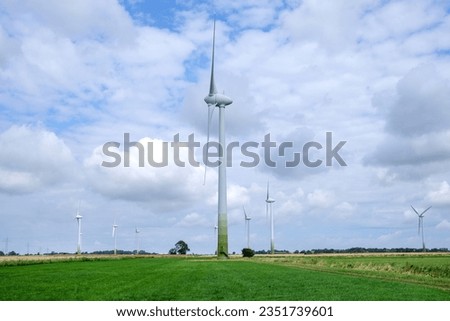 Concept of sustainable and alternative energy: Side view of several huge wind turbines and electricity pylons with power lines in a rural area with fields and trees, lot of copy space