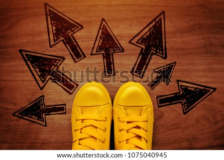 Concept of taking the right decision for the future, top view of young person wearing yellow casual sneakers standing over the arrow impints on wooden surface.
