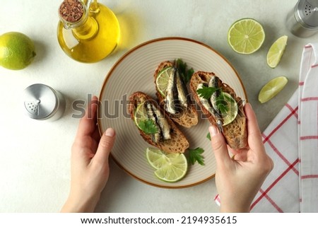 Concept of tasty snack with sandwiches with sprats on light textured background