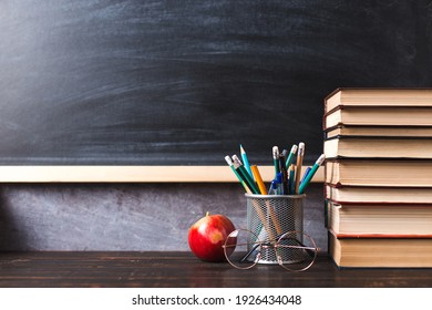 Concept to teacher's day. Pens, apple, pencils, books and glasses on the table, against the background of chalkboard. Back to school, copy space. - Shutterstock ID 1926434048