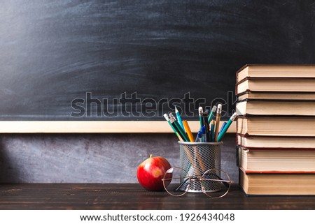 Concept to teacher's day. Pens, apple, pencils, books and glasses on the table, against the background of chalkboard. Back to school, copy space.