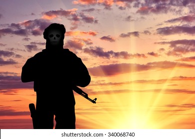 Concept of terrorism. Silhouette of a terrorist with weapons and a skull face at sunset
