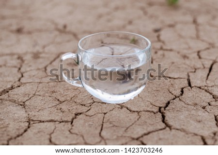 Concept of thirst, dehydration, lack of water. A cup of water on cracked dry ground.