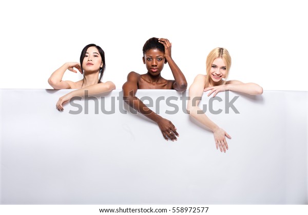 白い空のパネルの上に 空き地で笑顔を見せ 裸で見える アジア人 アフリカ人 白人の3人の異なる民族性女性を持つコンセプト の写真素材 今すぐ編集